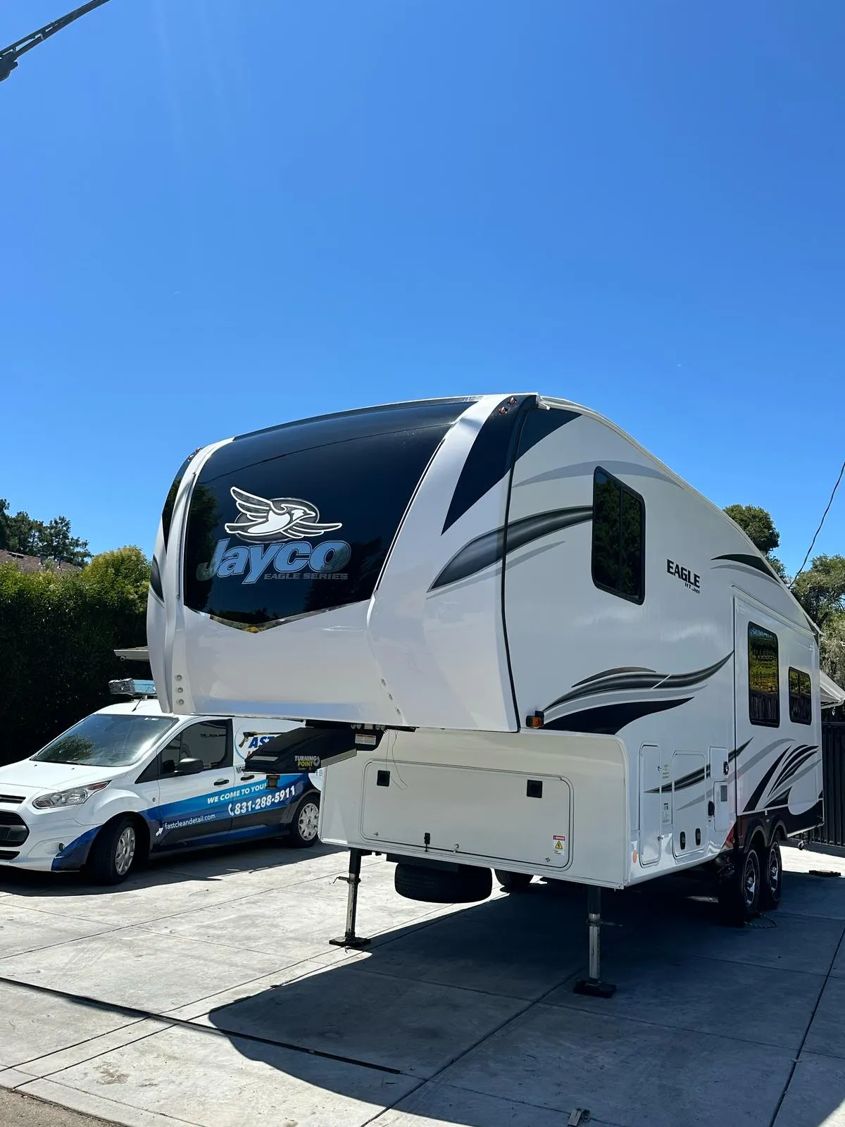 Fifth wheel travel trailer parked in a driveway next to the Fast Clean Mobile Detailing branded van.