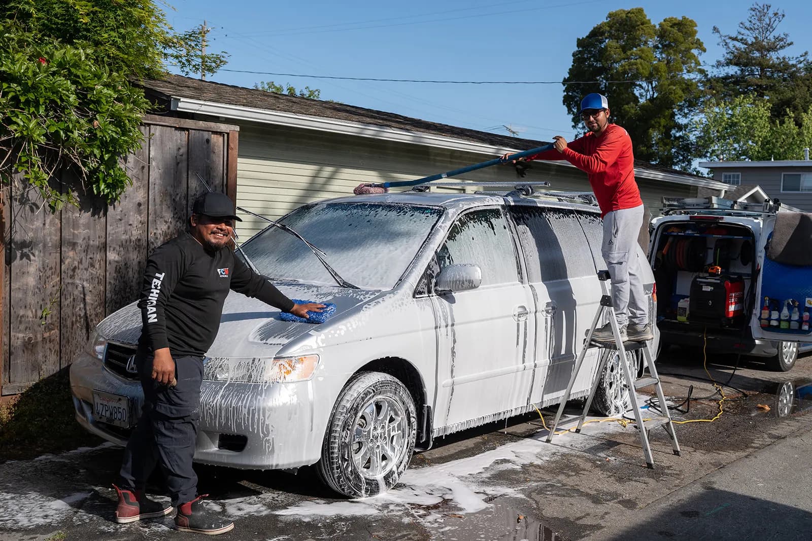 Fast Clean Mobile Detailing technicians washing a minivan in a residential driveway.