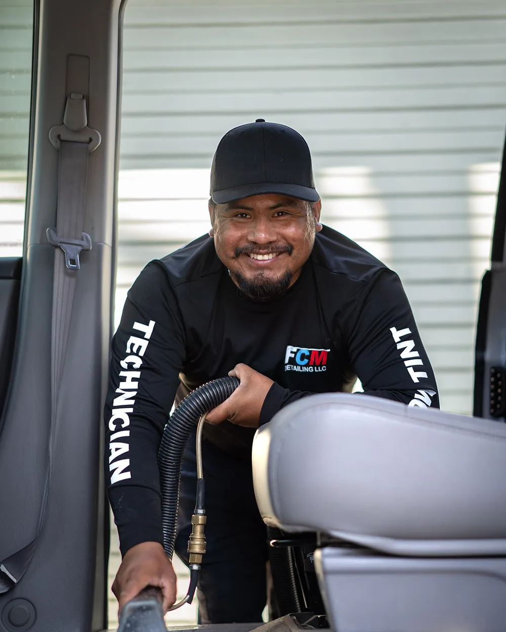 Jesus Gonzalez, owner of Fast Clean Mobile Detailing, smiling while detailing a vehicle's interior with a steam hose.
