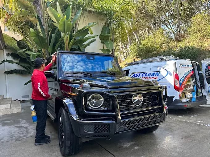 Fast Clean technician detailing a black Mercedes-Benz G-Wagon in a driveway, with the Fast Clean service van parked behind it.