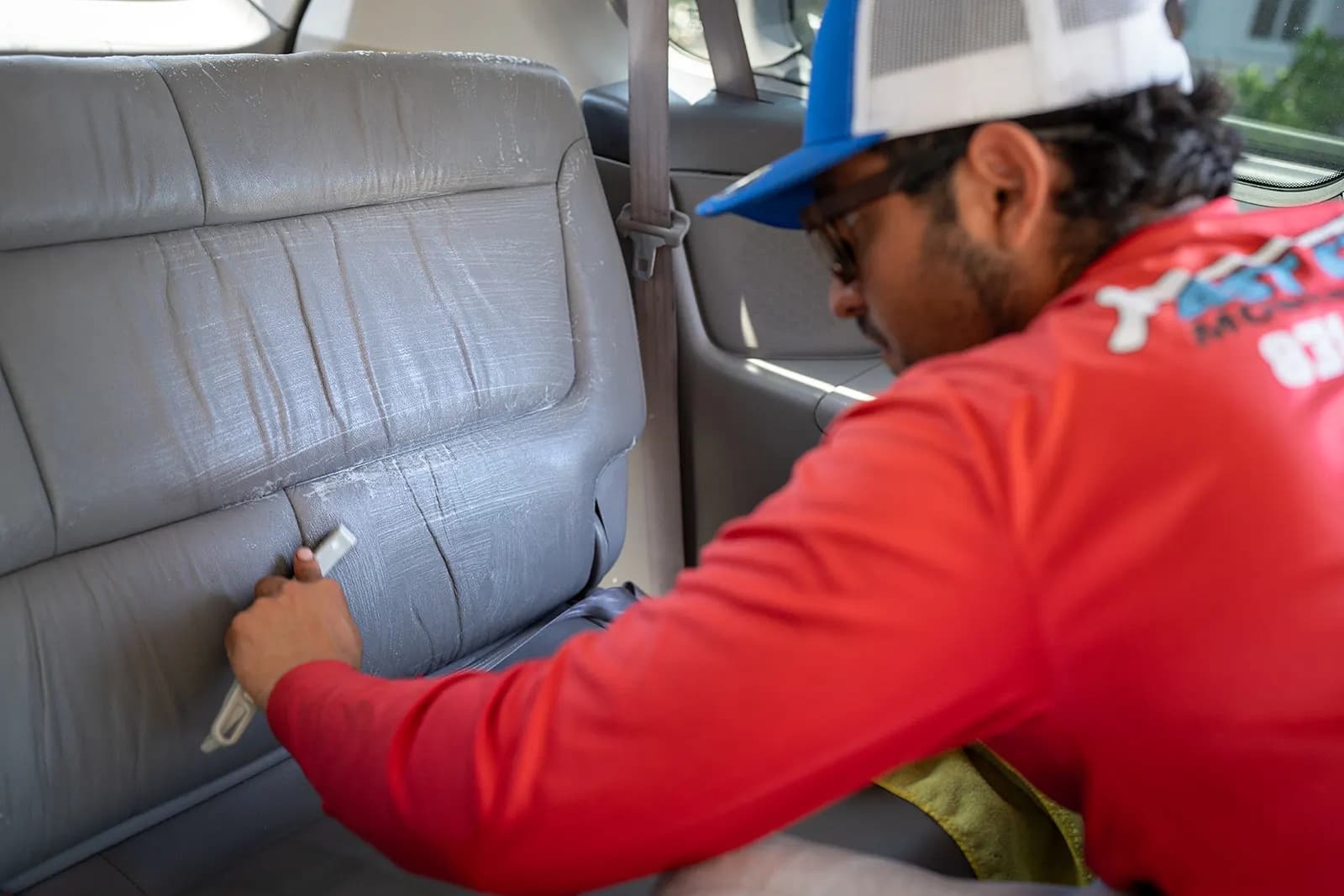 Fast Clean technician cleaning a rear vehicle seat with a detailing brush inside a car's interior.