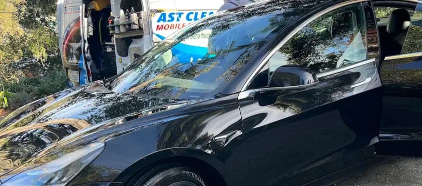Black Tesla Model 3 parked next to the Fast Clean Mobile Detailing branded van after a mobile detail.
