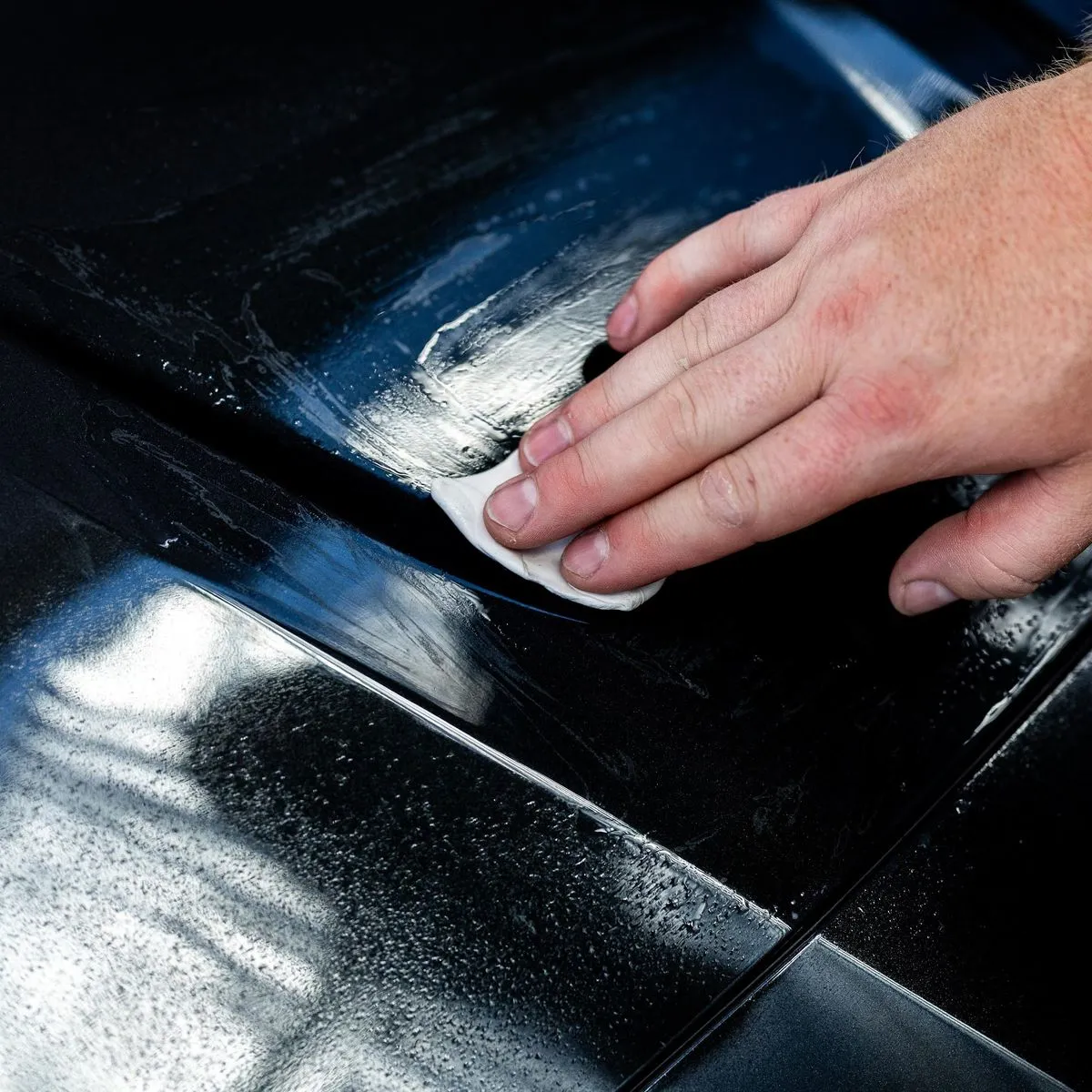 Detailer using a white clay bar to remove contaminants from black car paint.