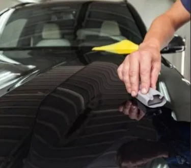 Detailer applying wax to a black car hood using a professional applicator pad.